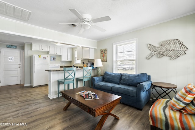 living room with dark wood-style floors, ornamental molding, a ceiling fan, and a textured ceiling