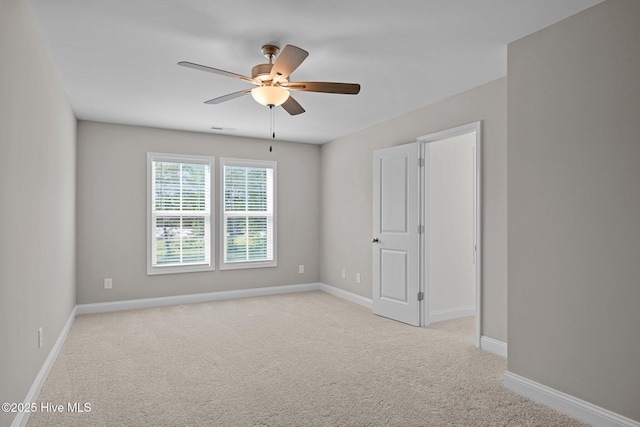 empty room featuring a ceiling fan, light colored carpet, and baseboards