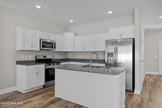 kitchen featuring appliances with stainless steel finishes, a sink, white cabinetry, dark stone counters, and recessed lighting