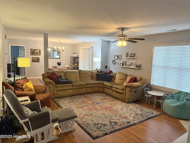 living area featuring a chandelier, wood finished floors, ceiling fan, and a textured ceiling