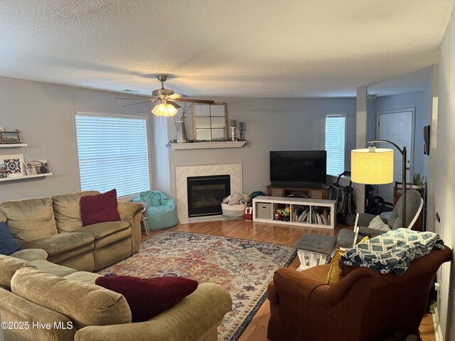 living area featuring a premium fireplace, a ceiling fan, wood finished floors, and a textured ceiling