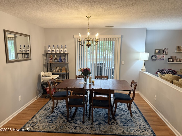 dining space with a chandelier, wood finished floors, a textured ceiling, and baseboards