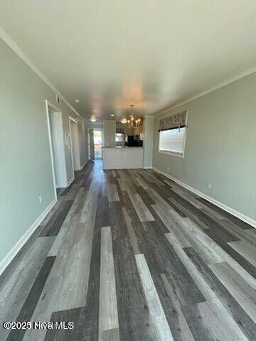 unfurnished living room with a chandelier, plenty of natural light, dark wood finished floors, ornamental molding, and baseboards