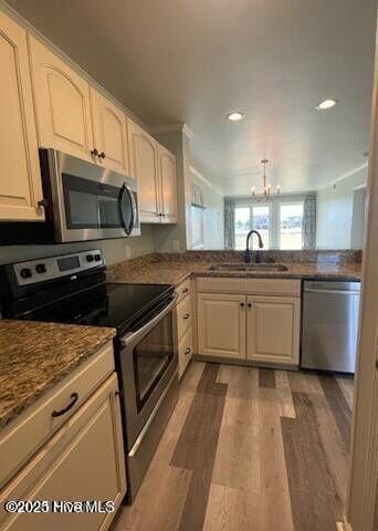 kitchen featuring appliances with stainless steel finishes, a chandelier, a sink, wood finished floors, and recessed lighting