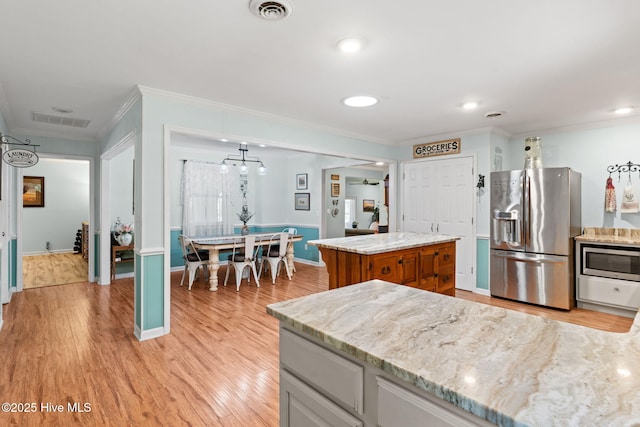 212 Park Ave, Southport, NC 28461 - kitchen featuring appliances with stainless steel finishes, crown molding, light wood-style floors, brown cabinetry, and light stone counters