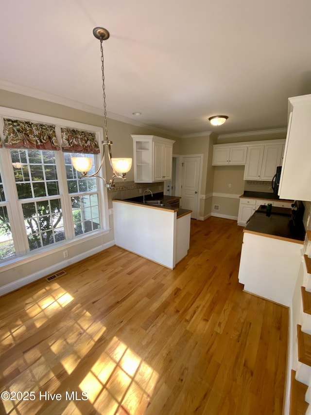 kitchen with dark countertops, crown molding, a peninsula, white cabinets, and light wood-type flooring