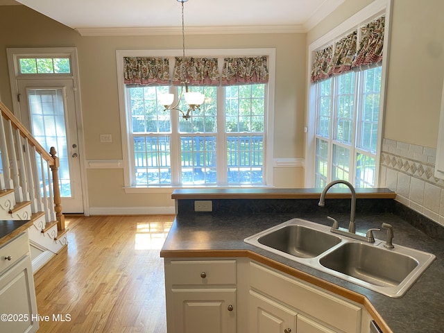 kitchen with a sink, dark countertops, healthy amount of natural light, crown molding, and light wood-style floors