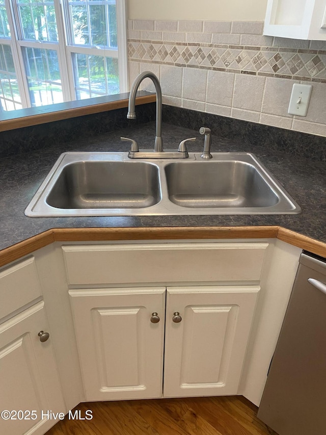 kitchen view of a sink, stainless steel dishwasher, dark countertops, and white cabinetry