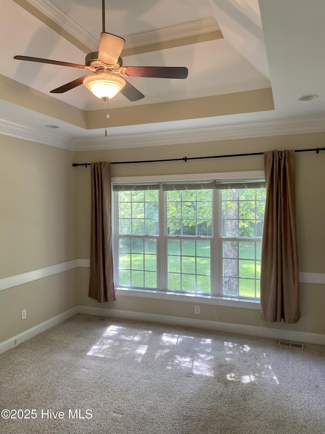 carpeted empty room featuring a tray ceiling, crown molding, a ceiling fan, and baseboards