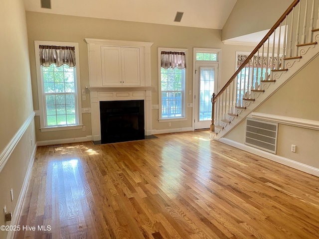 unfurnished living room with light wood finished floors, stairs, lofted ceiling, a fireplace with flush hearth, and baseboards