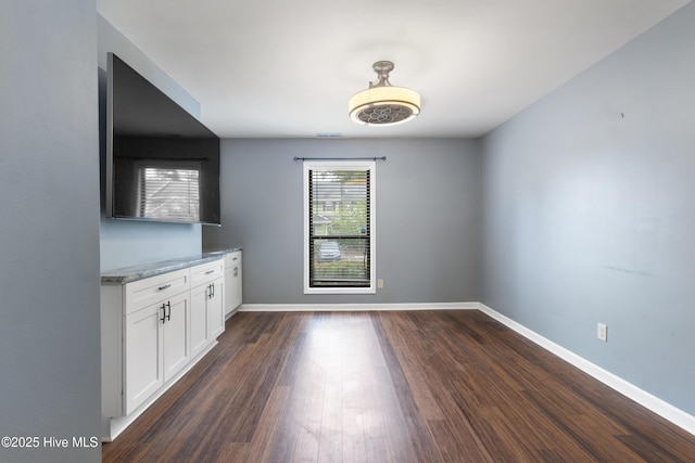 unfurnished dining area featuring baseboards and dark wood-type flooring