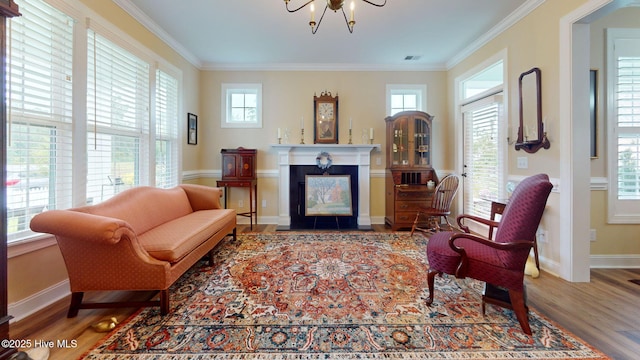 sitting room featuring wood finished floors, a fireplace with flush hearth, crown molding, a chandelier, and baseboards