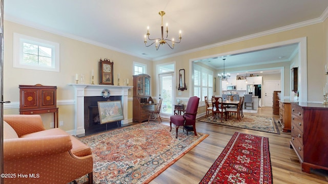 living room featuring a chandelier, light wood-type flooring, healthy amount of natural light, a fireplace, and crown molding