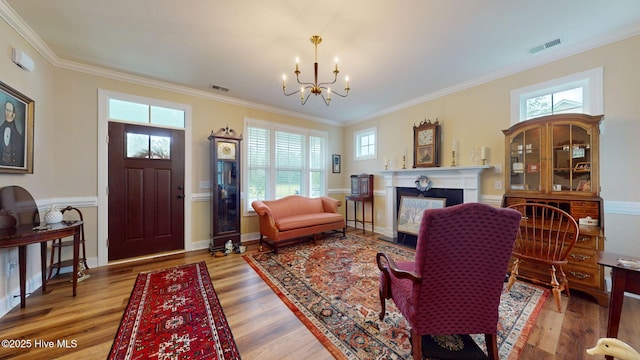 living area featuring a chandelier, wood finished floors, ornamental molding, a fireplace with flush hearth, and baseboards