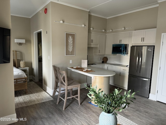 kitchen with freestanding refrigerator, wood finished floors, backsplash, light countertops, and ornamental molding