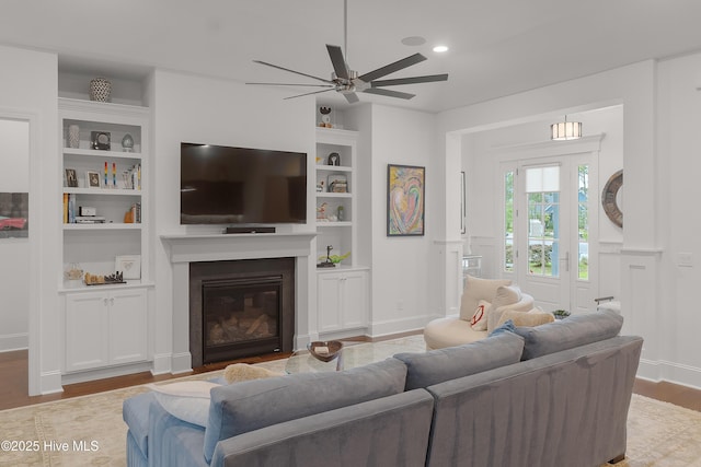3752 Glenmere Ln, Southport, NC 28461 - living area with built in shelves, ceiling fan, wood finished floors, a glass covered fireplace, and a decorative wall