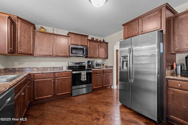 606 Spoleto Ct, Swansboro, NC 28584 - kitchen featuring appliances with stainless steel finishes, dark wood-type flooring, arched walkways, a sink, and a textured ceiling