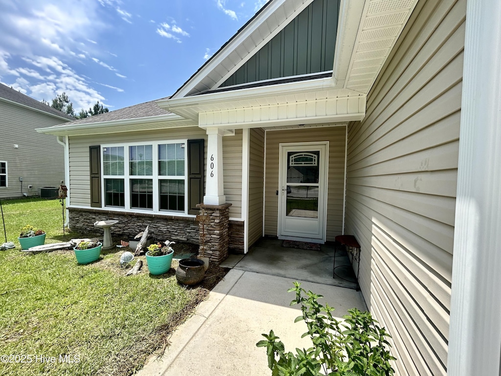doorway to property featuring board and batten siding, central AC unit, stone siding, a yard, and covered porch