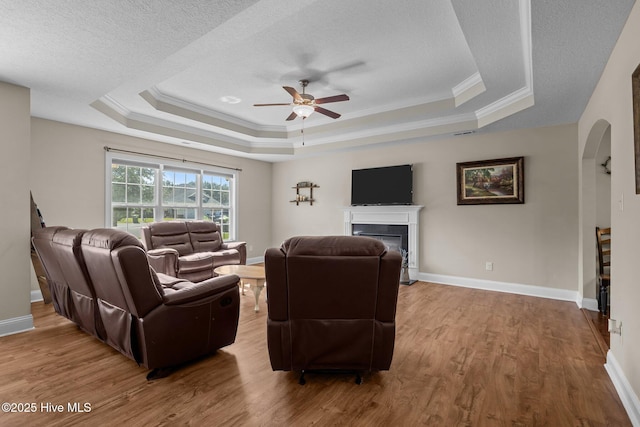 606 Spoleto Ct, Swansboro, NC 28584 - living room featuring a ceiling fan, a fireplace, wood finished floors, arched walkways, and a tray ceiling