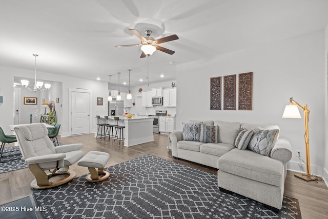 living room featuring ceiling fan, light wood finished floors, a chandelier, baseboards, and recessed lighting