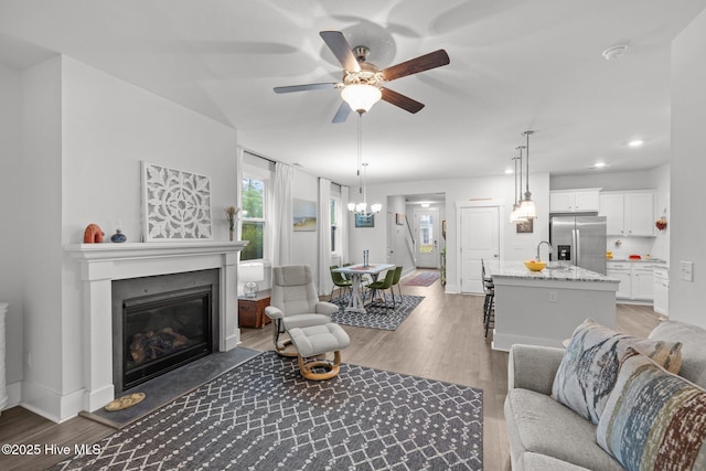living area with light wood-style floors, ceiling fan, a glass covered fireplace, a chandelier, and baseboards