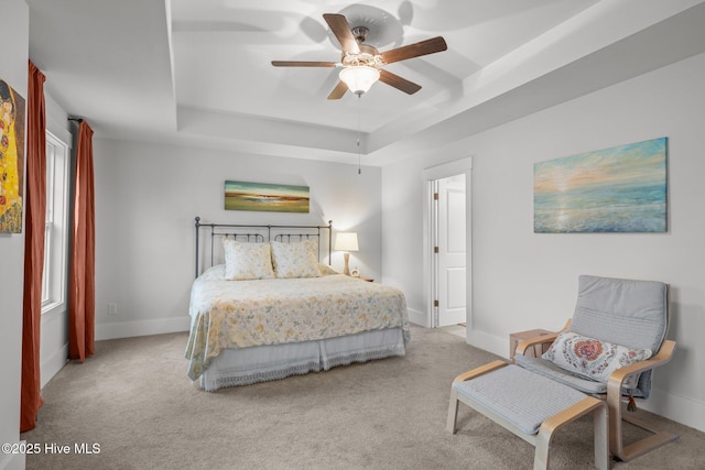 carpeted bedroom with a raised ceiling, baseboards, and a ceiling fan