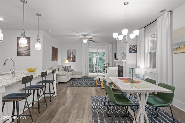 dining room featuring wood finished floors, a fireplace, ceiling fan, baseboards, and a chandelier