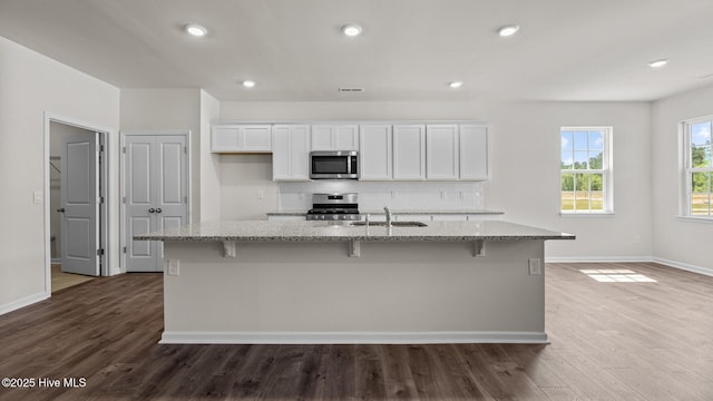 kitchen with stainless steel appliances, a sink, white cabinetry, light stone counters, and recessed lighting