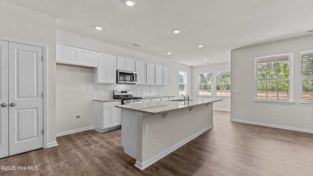 kitchen featuring appliances with stainless steel finishes, white cabinetry, dark wood-style flooring, light stone counters, and recessed lighting