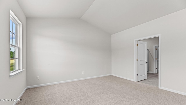 unfurnished bedroom with light carpet, multiple windows, vaulted ceiling, and baseboards