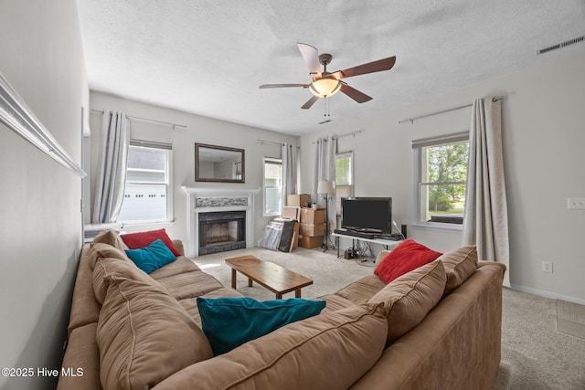living room featuring carpet floors, ceiling fan, a premium fireplace, a textured ceiling, and baseboards