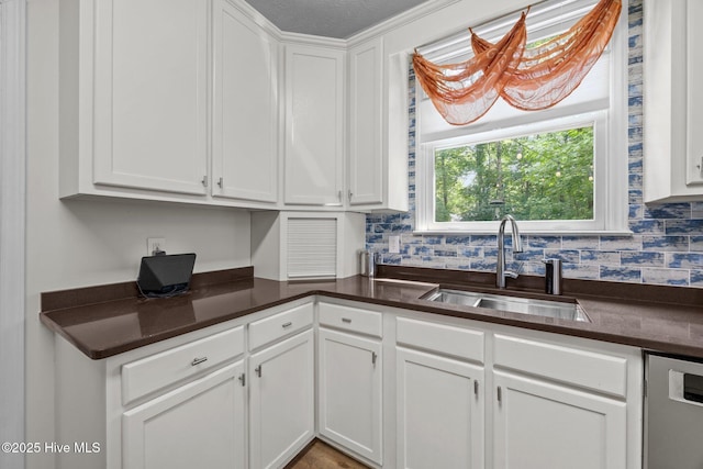 kitchen with a sink, dark countertops, white cabinetry, tasteful backsplash, and stainless steel dishwasher