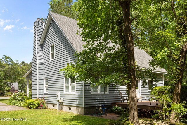 view of property exterior featuring roof with shingles, a wooden deck, a chimney, and a yard