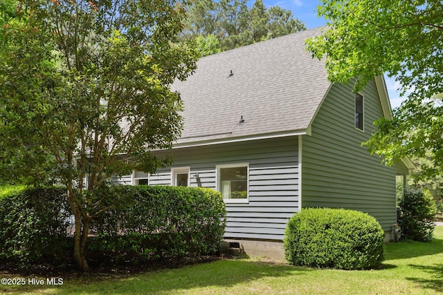 view of side of home with a shingled roof and a lawn