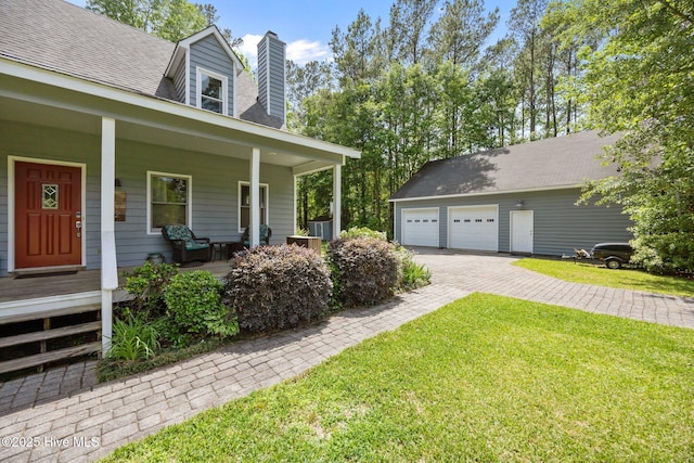 view of side of property featuring a porch, an outdoor structure, a detached garage, a chimney, and a lawn