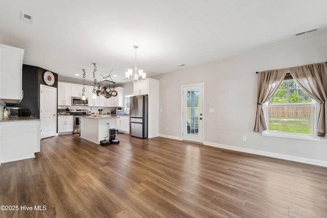 unfurnished living room with a chandelier, healthy amount of natural light, dark wood-style floors, and baseboards