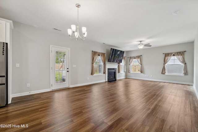 unfurnished living room with dark wood finished floors, a chandelier, a ceiling fan, and healthy amount of natural light
