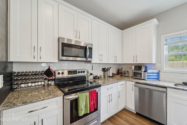 kitchen featuring appliances with stainless steel finishes, white cabinets, backsplash, and light wood-style flooring