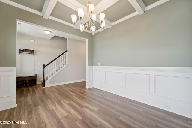 empty room with stairway, beam ceiling, a chandelier, coffered ceiling, and wood finished floors