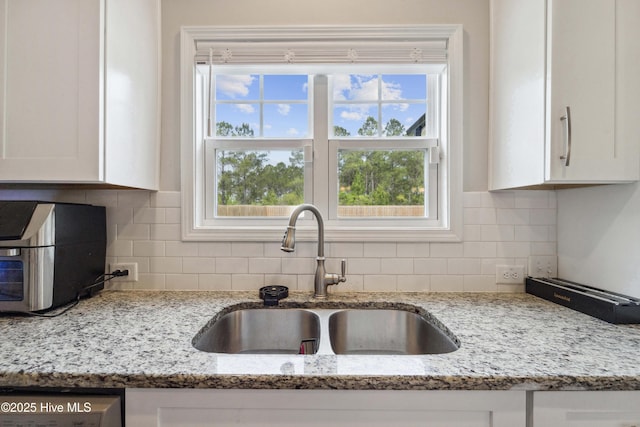 kitchen featuring a sink, white cabinetry, decorative backsplash, and light stone countertops