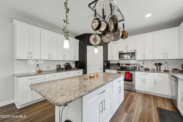 kitchen with appliances with stainless steel finishes, a center island, tasteful backsplash, wood finished floors, and white cabinets