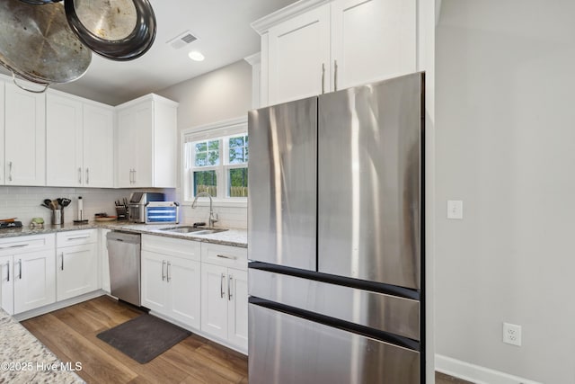 kitchen with stainless steel appliances, a sink, wood finished floors, backsplash, and white cabinetry