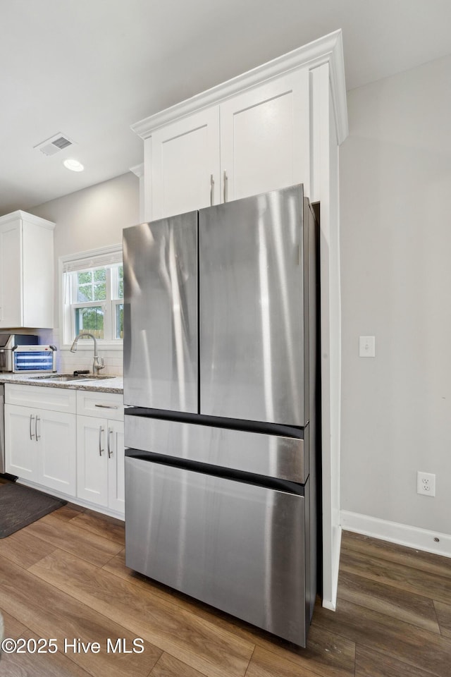 kitchen with freestanding refrigerator, white cabinetry, wood finished floors, a sink, and recessed lighting