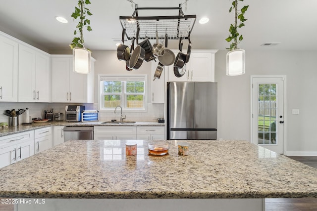 kitchen with stainless steel appliances, a sink, a center island, white cabinetry, and decorative backsplash