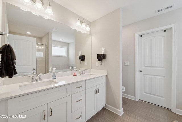 full bath featuring a stall shower, toilet, baseboards, and double vanity