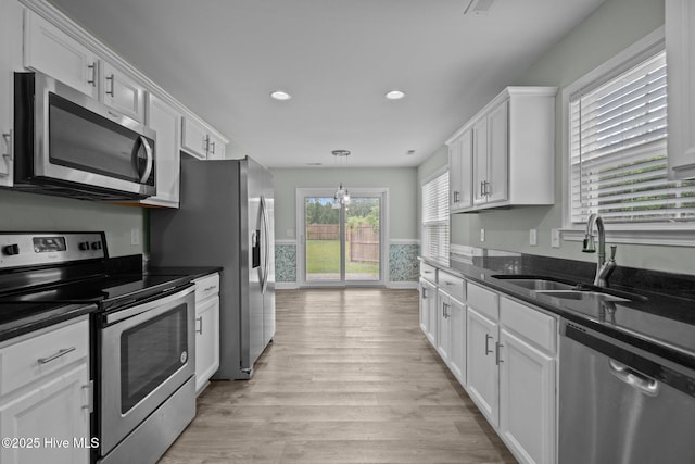 kitchen with appliances with stainless steel finishes, a sink, white cabinetry, light wood-style floors, and recessed lighting