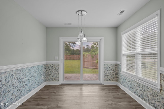 unfurnished dining area featuring wallpapered walls, wainscoting, baseboards, and wood finished floors