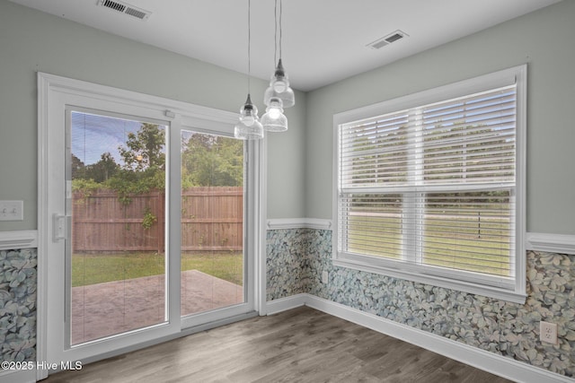 unfurnished dining area with healthy amount of natural light, baseboards, a chandelier, wood finished floors, and wallpapered walls