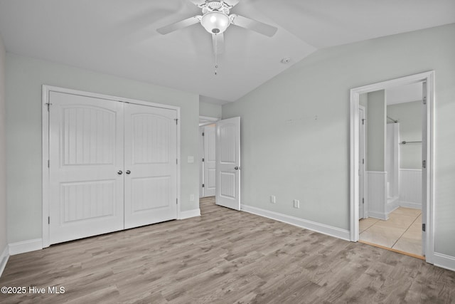 unfurnished bedroom featuring wood finished floors, vaulted ceiling, a closet, ensuite bathroom, and baseboards