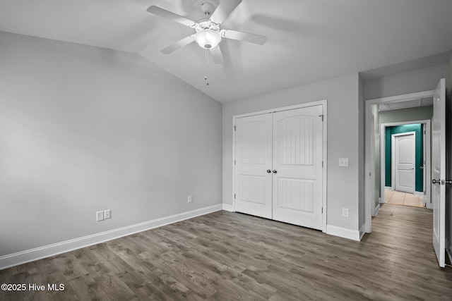 unfurnished bedroom featuring wood finished floors, a closet, baseboards, lofted ceiling, and ceiling fan